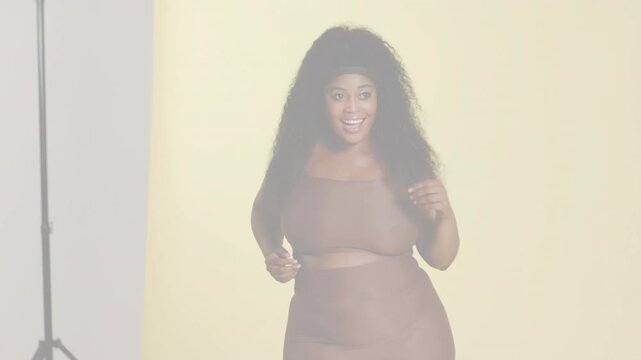 Female model responding to camera cue, adjusting crop top and dancing for playful fashion content