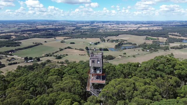 Aerial view of fire lookout tower above forest with wind turbines and rural landscape