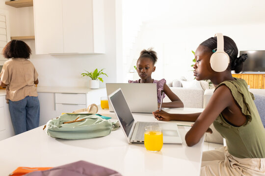 African American mom and daughters reacting to sun pouring OJ, using laptops for school, copy space