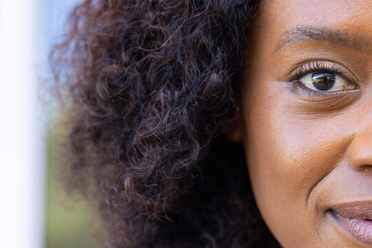 Adult African woman smiling after sunlight catching right eye and highlighting curly hair outdoors