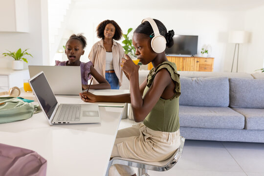 Vertical video: Class starting, teen girl in olive top wearing headset noting on laptop at kitchen