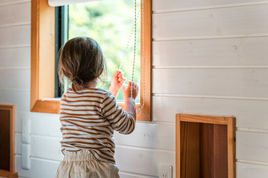 A mischievous girl's back as she plays by pulling on the cords of roller blinds and other blinds.