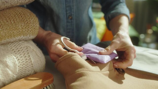 Close-up of hands attaching a scented sachet to a coat, part of a meticulous seasonal wardrobe organization and moth prevention routine for winter clothes.