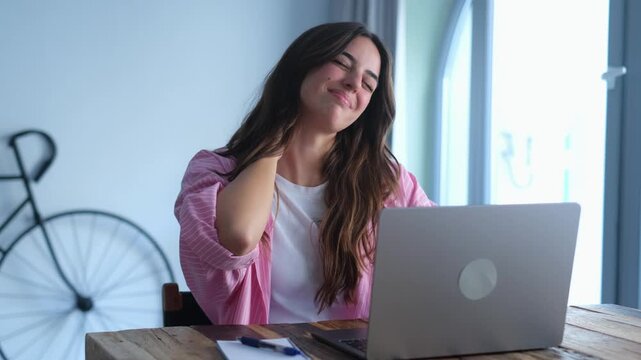 Tired woman feels neck pain, rubs tensed muscles seated at table, suffers from chronic shoulder back ache after long laptop usage, sedentary work, poor posture, health problems, fibromyalgia concept
