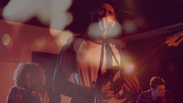 Lead singer stepping forward, strumming electric guitar, singing for music while flares drifting