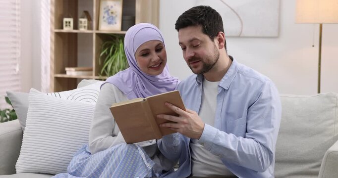 Happy muslim couple reading book on sofa at home