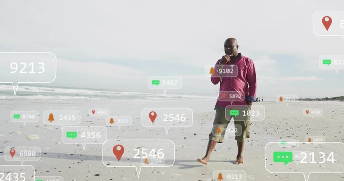Senior man walking along sandy beach while taking call, mobile tech alerts clustering around feet