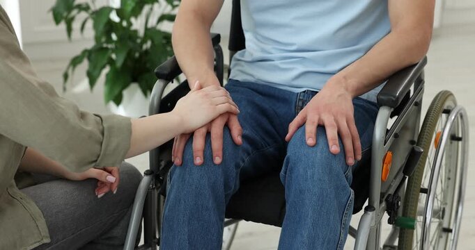 Woman supporting man in wheelchair at home, closeup