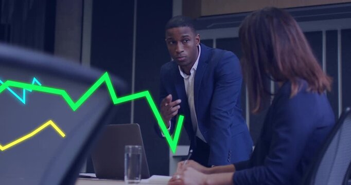 Standing man pointing at laptop, causing animated graphs to move while woman noting business trends