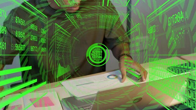 Analyst reaching notes and writing inspecting charts as green HUD analyzing finance data on laptop