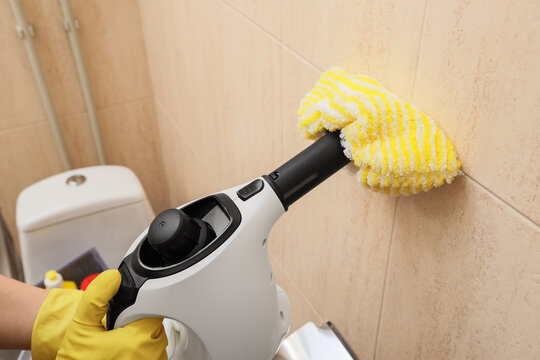 Female hands steam cleaning tile wall in restroom