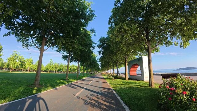 Tree-lined cycle path along coastal park with rose garden and sea view on sunny spring evening