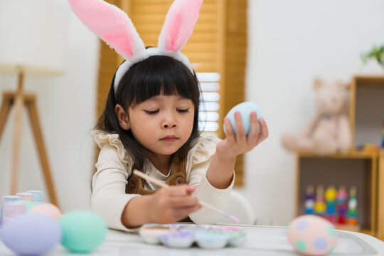 preschool child girl wearing bunny ears painting and decorating colorful egg at home on easter day