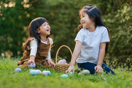 two happy child girl playing together and hunting for Easter eggs into basket on green grass in garden
