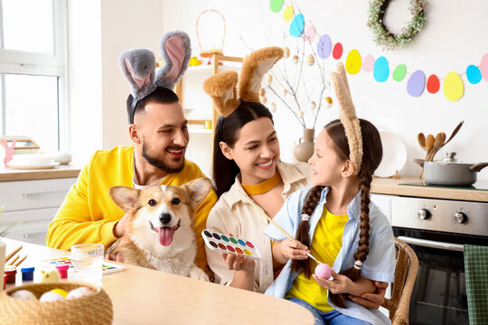 Happy parents with their little daughter and Corgi dog painting Easter egg in kitchen