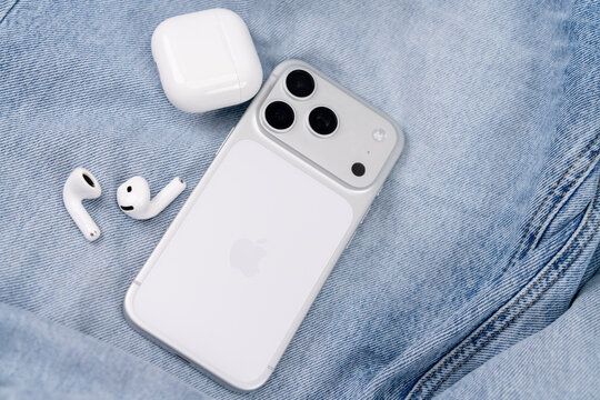 Bar, Montenegro: February 6, 2026: Silver Iphone 17 pro with a magnetic battery pack lies on blue jeans beside AirPods earbuds and charging case, modern mobile tech flat lay showing music listening
