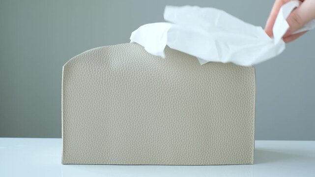 A hand pulls paper napkins out of box.