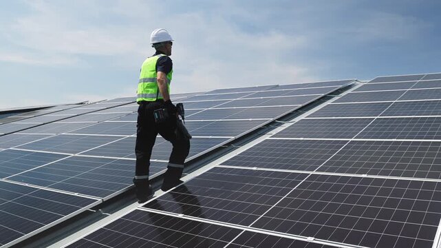 Technician installing solar panels on factory roof for green energy. A skilled technician in safety gear is working on a solar panel installation on rooftop. clean energy renewable power technology.