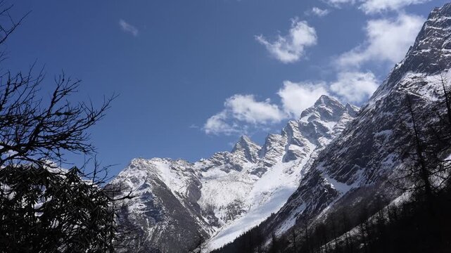 Snowy mountain peak alpine landscape in winter sky with cloud, rugged ridge above dark forest and valley view, fresh snowfall, bright sunlight on icy summit, serene cold wilderness panorama