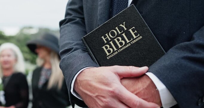 Hands, bible and pastor at cemetery for funeral, service and crowd with Christianity for mourning. People, priest and reverend with family, holy scripture or sermon for burial ceremony at graveyard