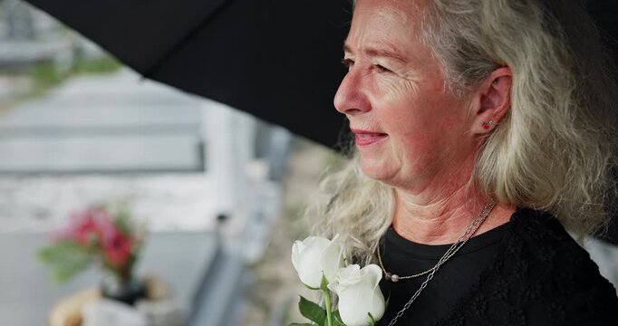 Senior, woman and umbrella at cemetery with flowers, grieving loved one and thinking about past memory. Sad, old person and reflection at graveyard outdoor with roses, mourning and sorrow for death.