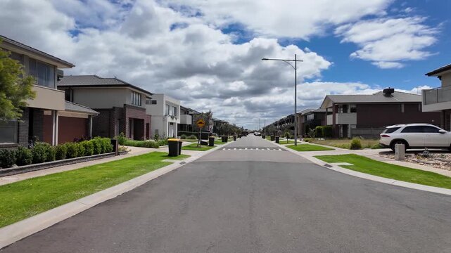 Wide residential street in Werribee South, Melbourne, Australia, with newly built modern houses and minimal tree coverage. An exposed suburban street in a new estate with young trees.