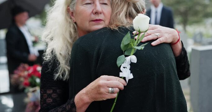 Sad, senior people and hug at graveyard for funeral ceremony, burial service and mourning loss. Family, embrace and elderly women with rose, emotional breakdown and condolences at farewell memorial