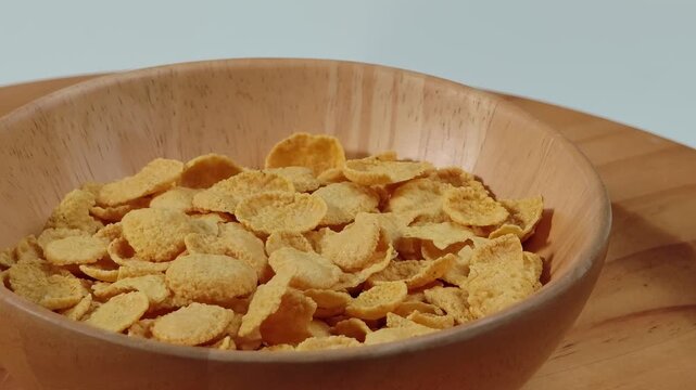 Cereal flakes pouring into a wooden bowl, breakfast cereal preparation