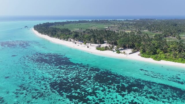 Wide-angle aerial shot of the tropical landscape on Thoddoo, Maldives, showcasing the contrast between the deep blue ocean and bright green vegetation.