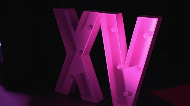 Closer view of a large illuminated XV sign decoration glowing in pink event lighting.