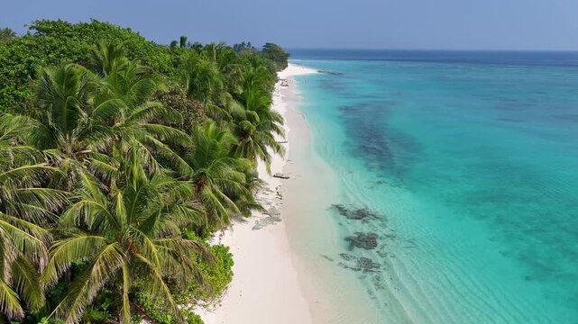 Stunning aerial view of a drone flying over the white sandy shore and lush green palm trees of Ukulhas Island, Maldives, revealing beautiful azure ocean water.