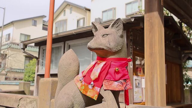 Stone fox statue with red bib at Japanese shrine in Tokyo city street