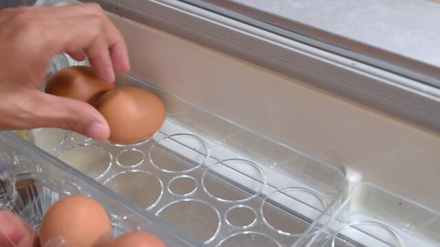 person hand picking eggs from pack and carefully placing into refrigerator door egg tray