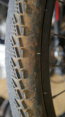 Close up of bicycle tire with chunky tread and dirt on the sidewall, mounted on a wheel with spokes shallow depth of field, workshop background.