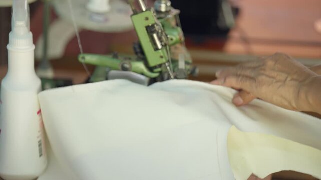 Industrial sewing machine stitching white fabric in garment factory. Close-up of textile manufacturing process showing clothing production, tailoring workflow and fashion industry craftsmanship.