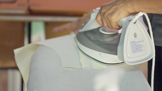 Close-up of clothing manufacturing process with fabric ironing before sewing. Professional garment production detail in textile industry highlighting apparel preparation and tailoring craft.