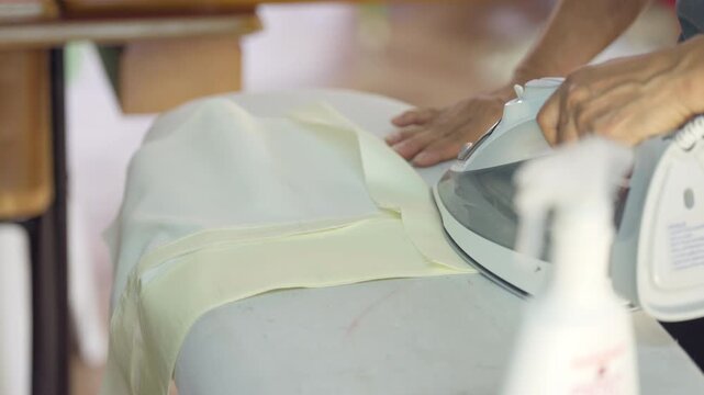 Garment fabric preparation using iron in textile workshop before sewing process. Clothing manufacturing stage in fashion industry highlighting apparel production and tailoring workflow.