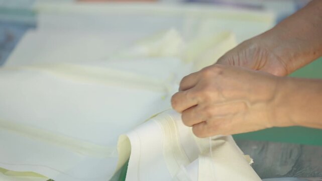 Close-up of professional tailor hands sewing white fabric in fashion design studio. Seamstress working carefully on garment production