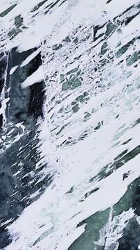 Overhead close-up of a boot footprint pressed into snow streaks over dark frozen glaze, creating a high-contrast abstract winter texture pattern for backgrounds, vertical.