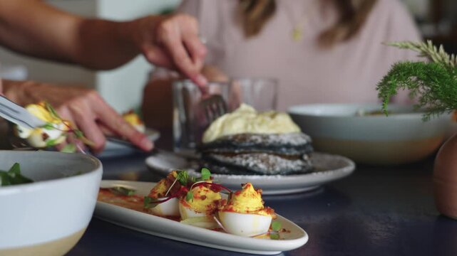 K footage of three women enjoying blue corn pancakes topped with cream and deviled eggs with microgreens during an elegant brunch setting with gourmet food and social dining.