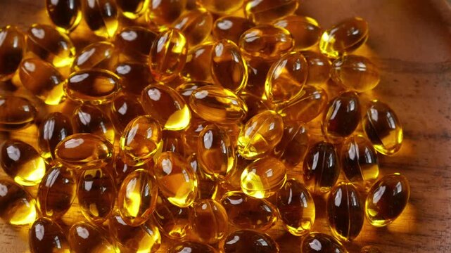Golden yellow fish oil omega-3 supplement softgel capsules piled on wooden plate, health nutrition vitamin dietary supplement concept