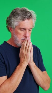 Mature man with grey hair praying on a green screen background