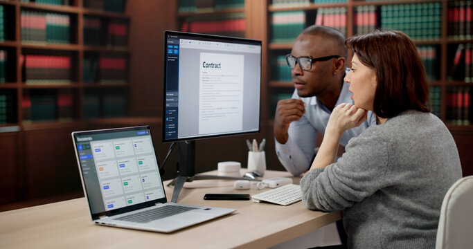 Two Lawyers And A Paralegal Carefully Review Contracts On Laptop Together
