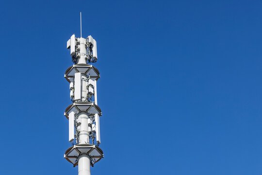 Telecommunication tower cell site with multiple mobile network antennas and transmitters for 5G and 4G in the future 6G signal coverage against clear blue sky.