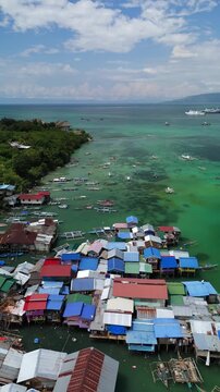 Vertical drone ascends and pulls back over stilt houses and outrigger boats on Panglao Channel in Bohol