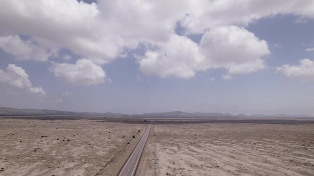 A vast west Texas desert landscape with an empty highway cutting through it, aerial view of the desert and high clouds