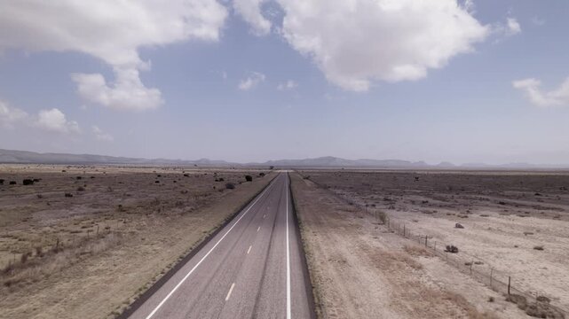 A vast west Texas desert landscape with an empty highway cutting through it, fast moving aerial view