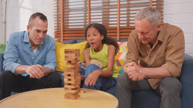 Caucasian senior gay couple playing wood block game with adopted daughter