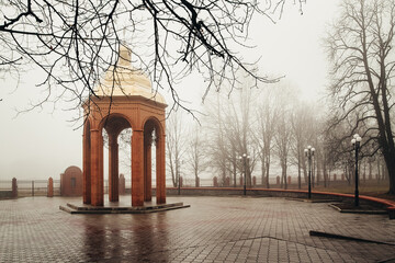 Brick gazebo with a golden dome in a foggy city park during autumn