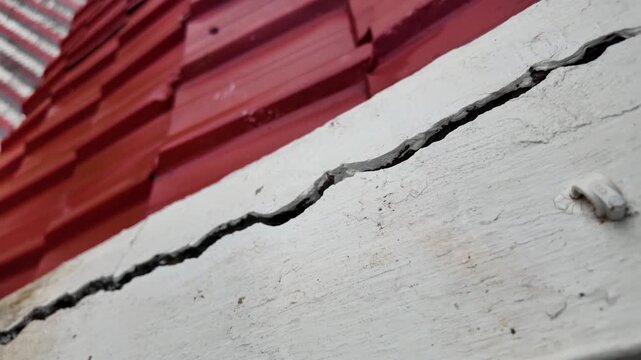 Large Crack in White Concrete Wall Near Red Roof